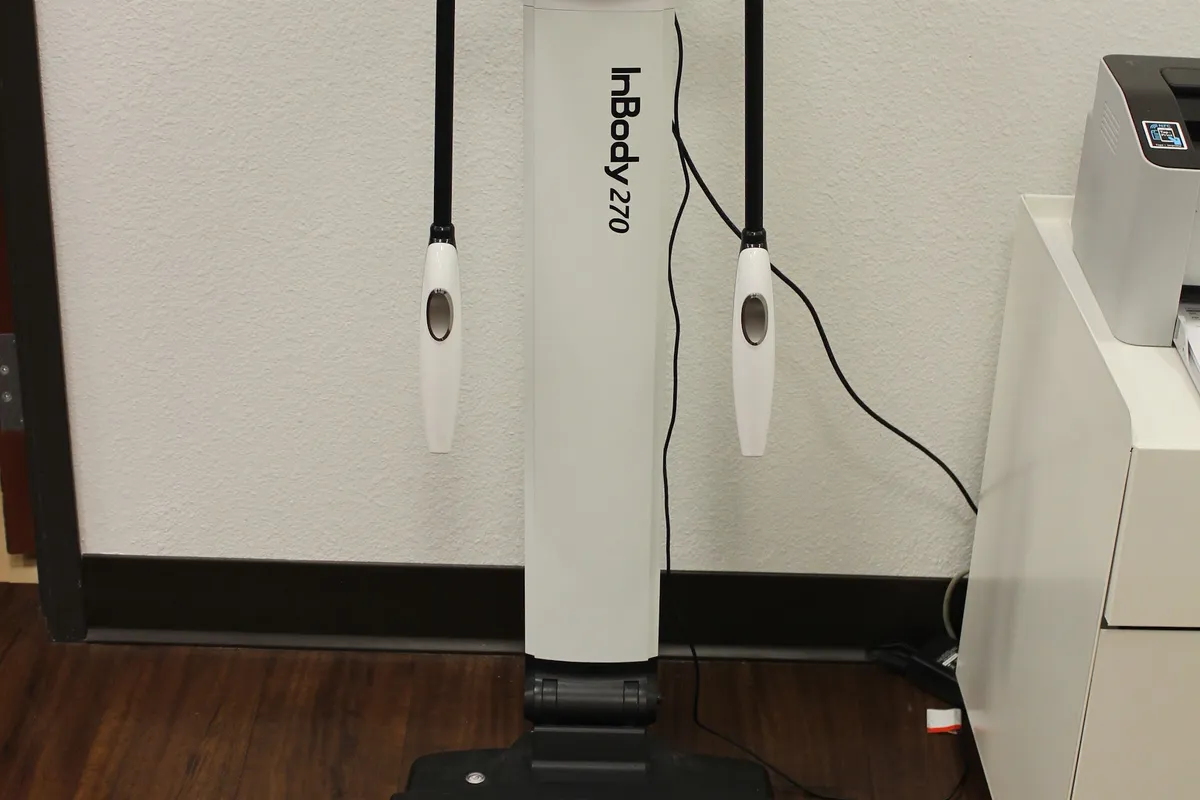 The InBody 270 body-composition analyser standing against a wall, its two hand grips hanging at either side.
