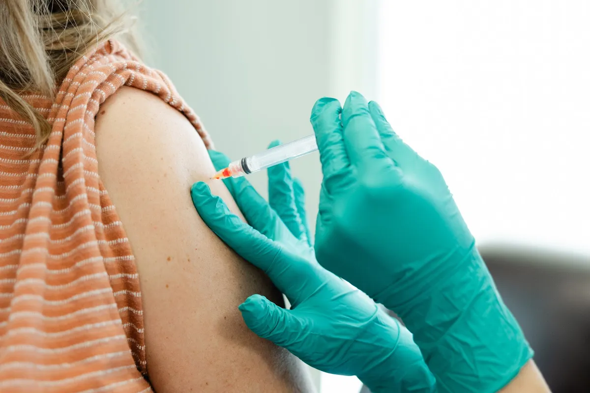 A gloved intramuscular injection given in the upper arm