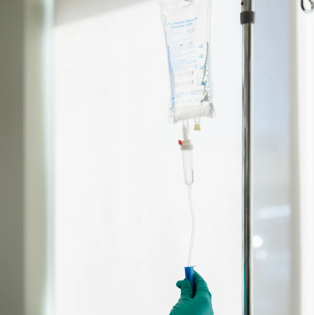 An IV bag hung on the stand, a gloved hand adjusting the line