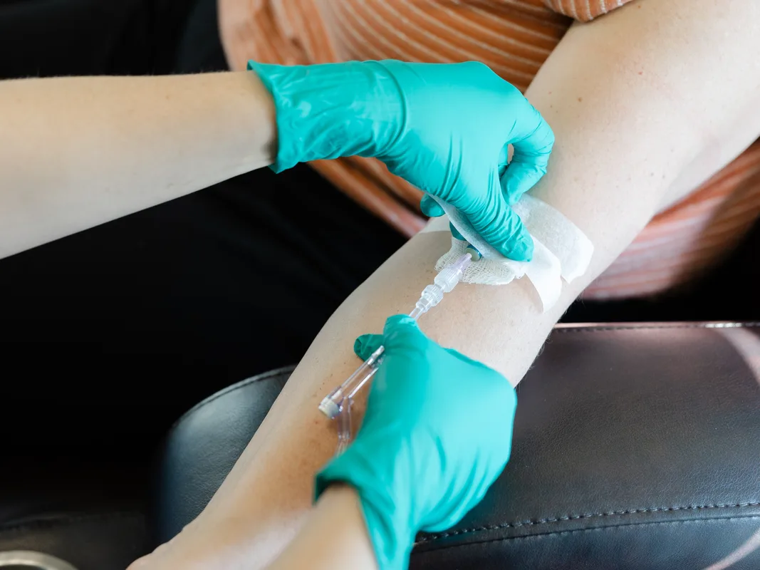Gloved hands connecting an IV line at a client's arm