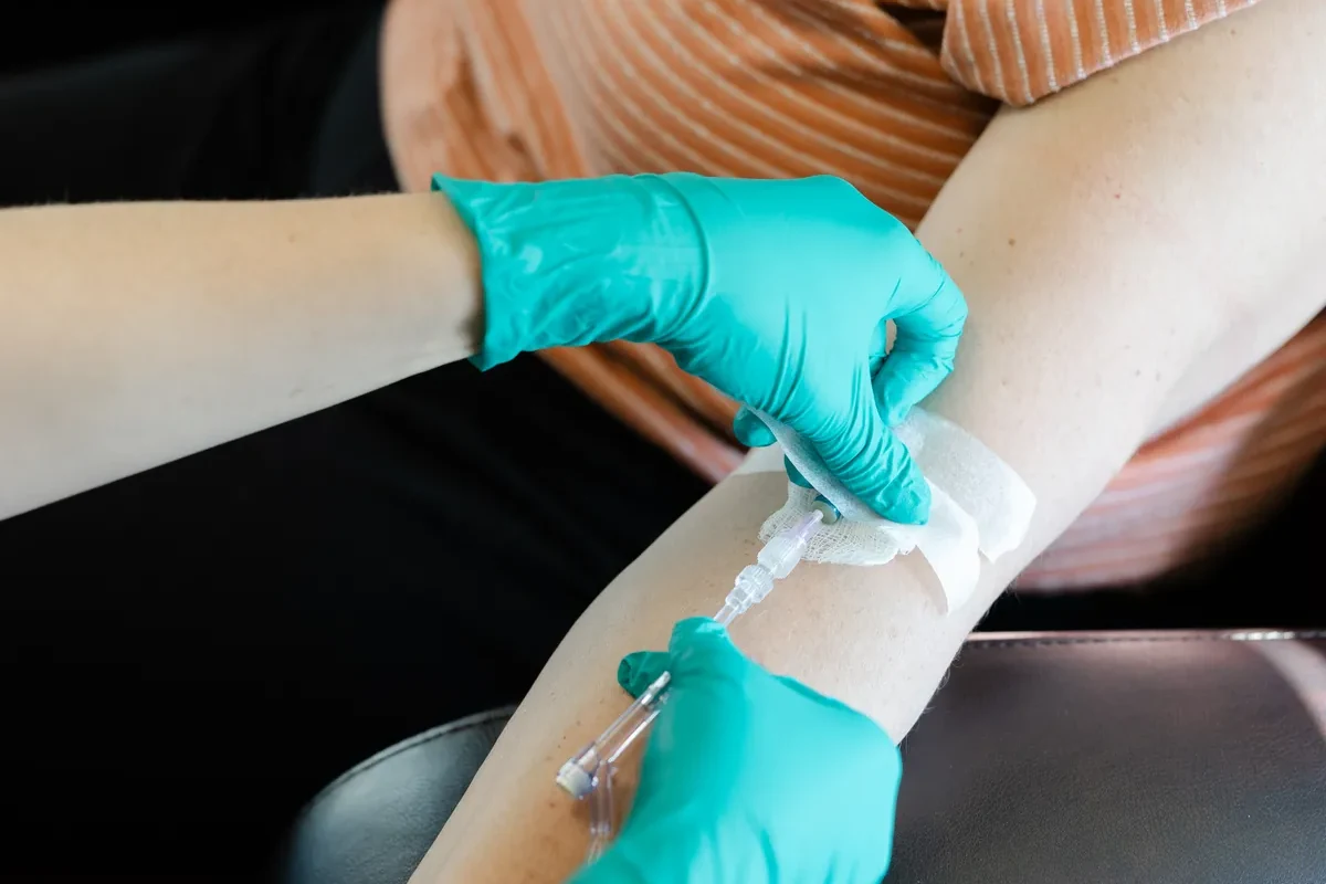 Gloved hands securing an IV line taped at a client's forearm