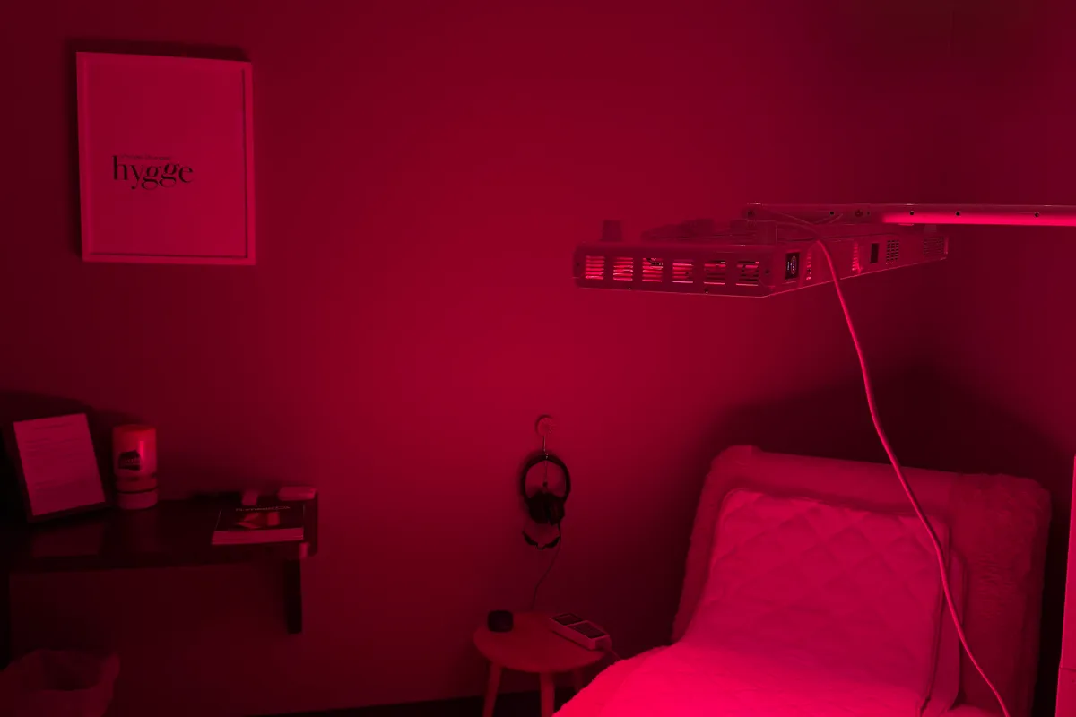 The red light room lit deep red, a hinged light panel angled above a padded bed with headphones hanging on the wall beside it.