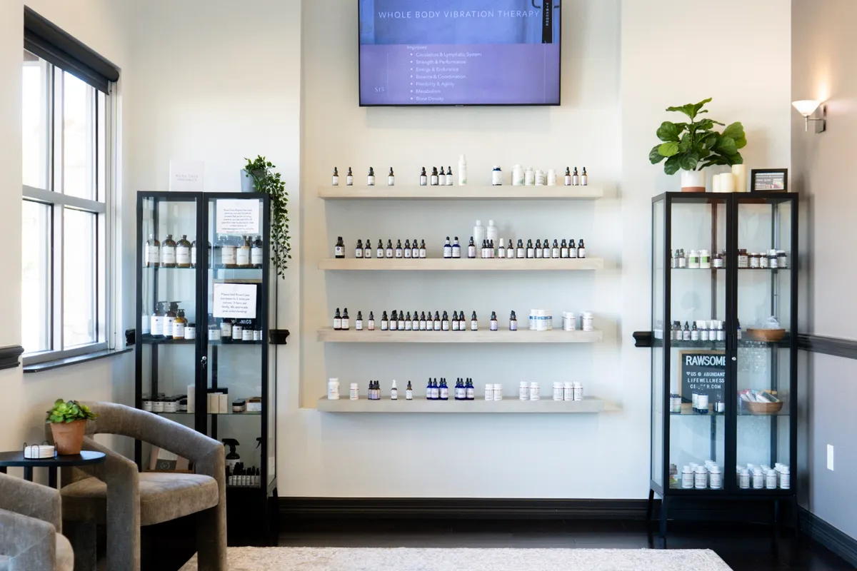 A tall, light room lined with shelves of tinctures and supplement bottles, a glass display cabinet on each side and an armchair by the window.