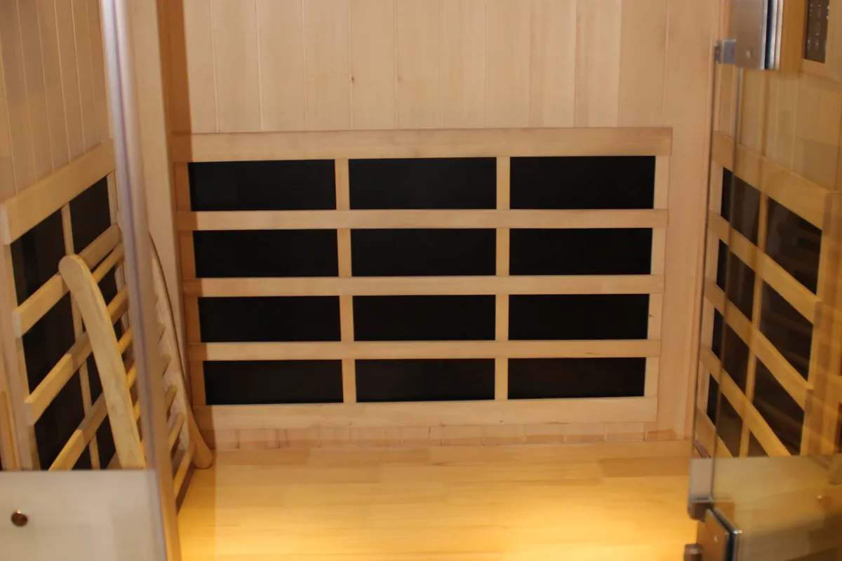Inside the cedar infrared sauna — black heater panels behind a slatted bench and a wooden chair.