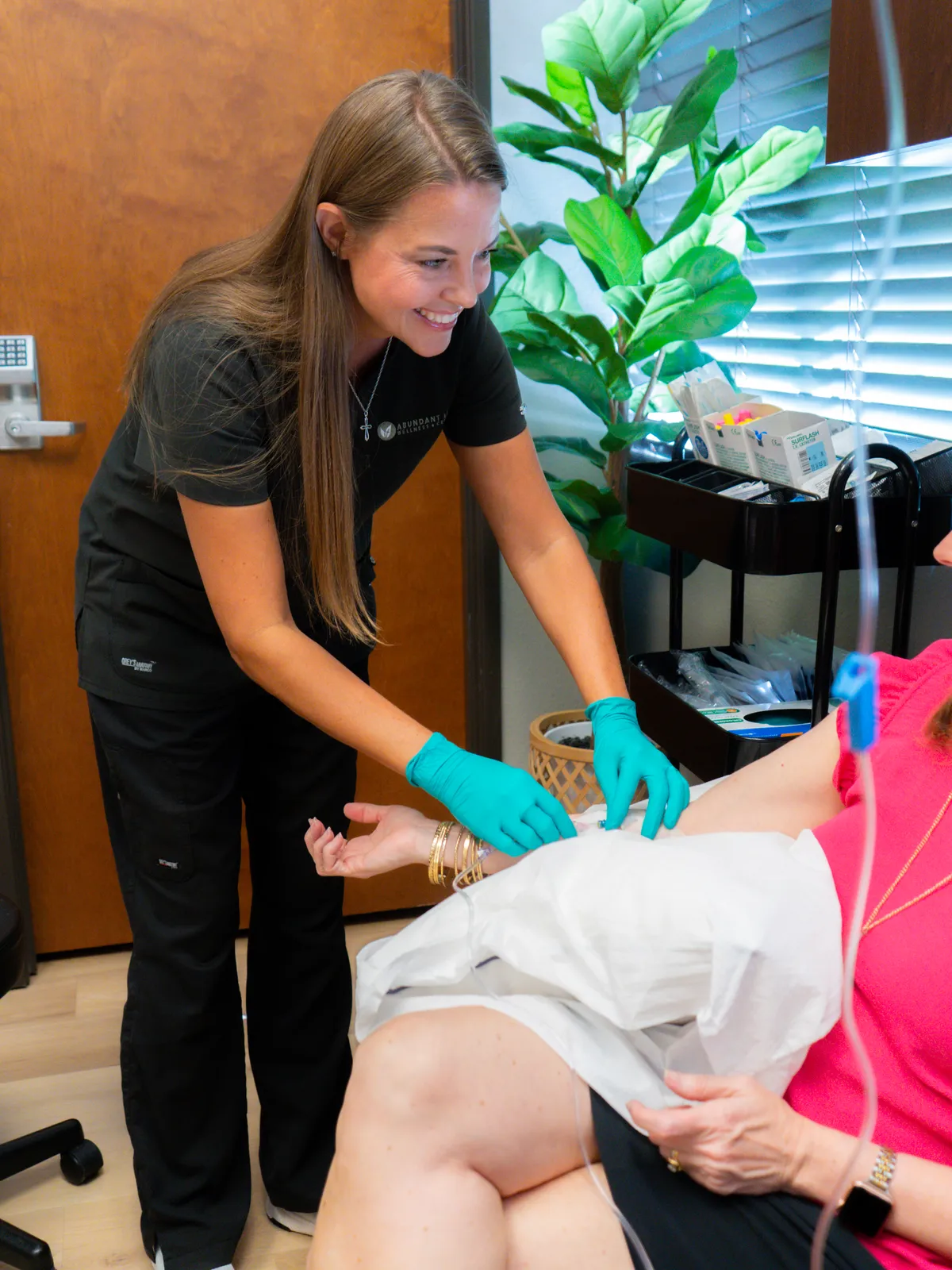 A nurse leaning in at a seated client's arm in the IV room