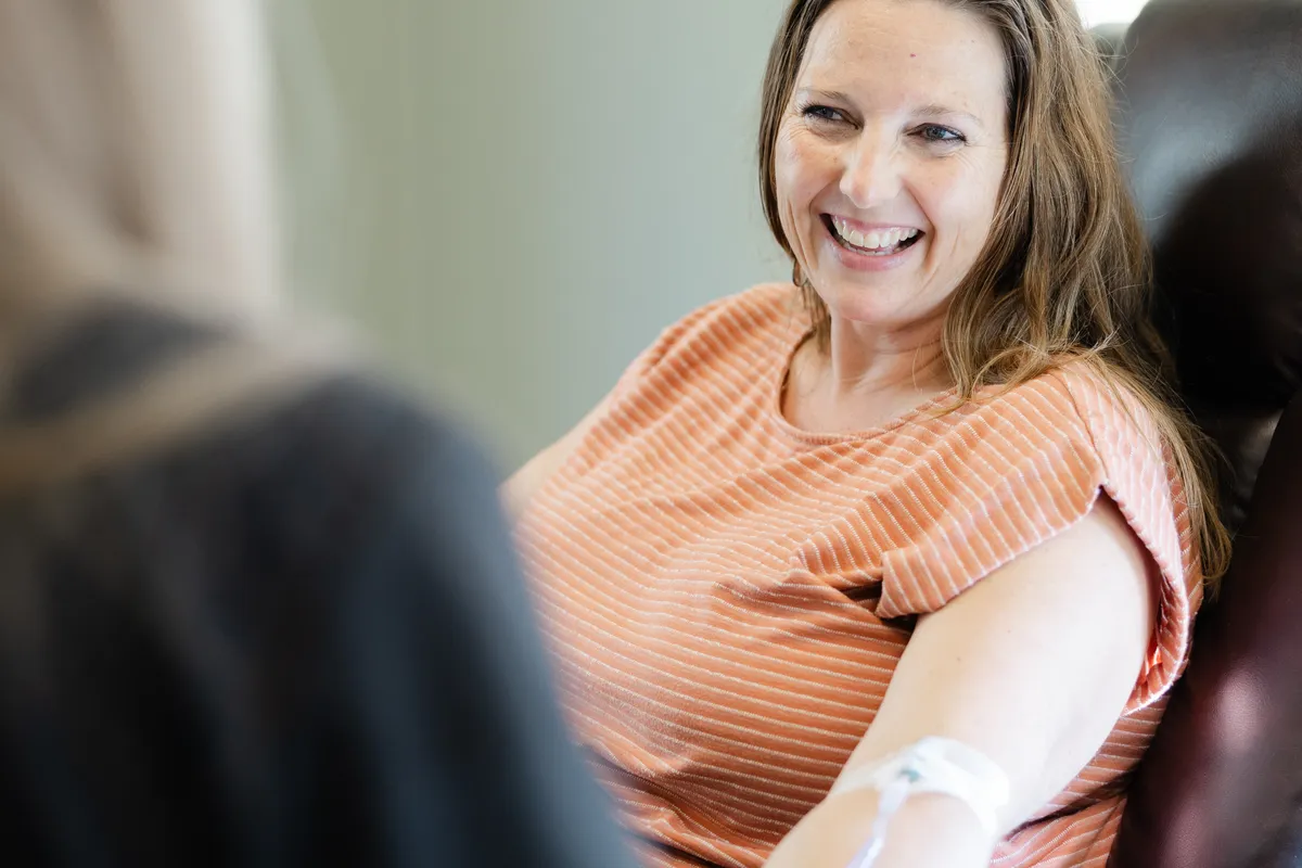 One of our nurses, smiling, with gloved hands on a client's upper arm before a vitamin shot